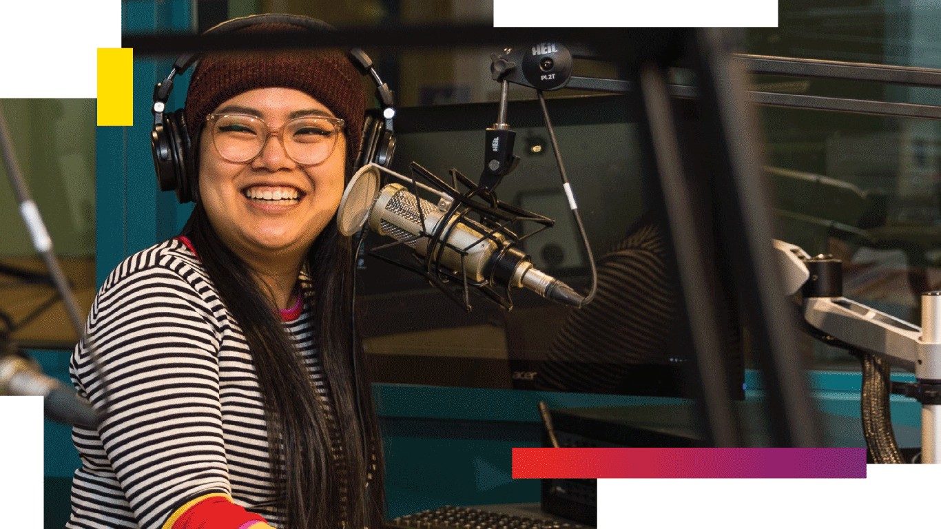 Student laughing while sitting at an audio desk with microphone
