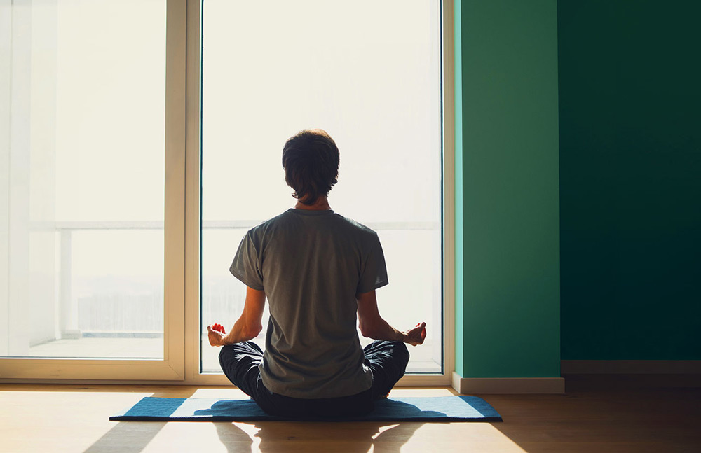 Back of a man sitting cross-legged in front of a window