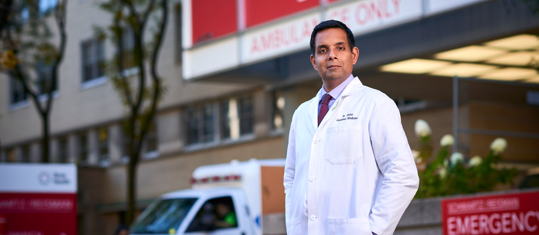 Dr. Samir Sinha in a doctor's coat, standing outside a hospital emergency department