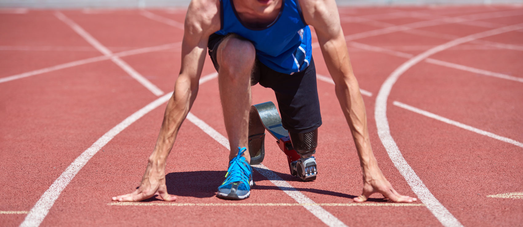 Close-up of an athlete with a prosthetic leg kneeling at the starting line of a running track