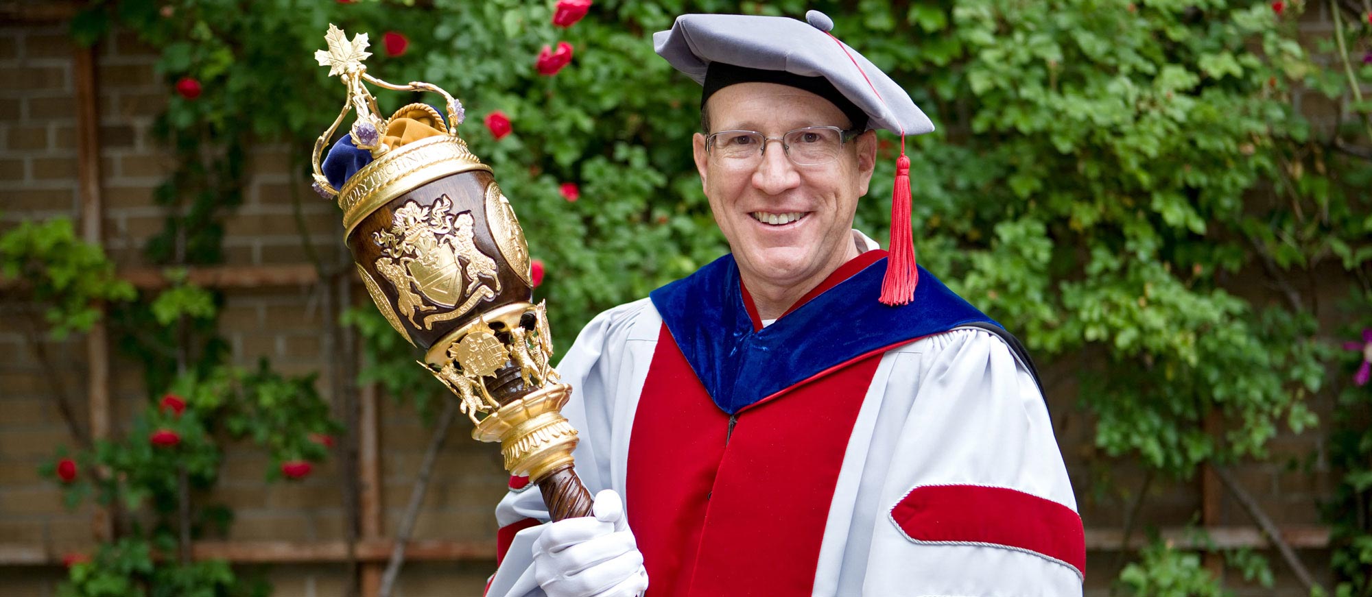 Dr. Steven Gedeon dressed in academic regalia and holding an ornate staff