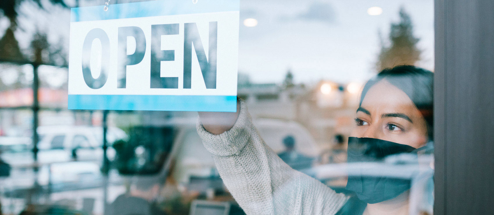 Woman wearing a face mask hanging an open sign on the window of her store